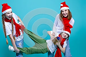 Seasonal Holidays Ideas. Three Positive Caucasian Girls With Santa Hats Having Fun While Lifting Teenage Girl Holding Wrapped Gift