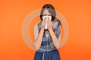 Seasonal influenza. Portrait of flu-sick brunette woman wrapped in scarf, blowing her nose and sneezing in napkin