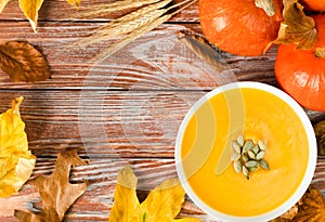 Seasonal pumpkin soup, autumn leaves and pumpkins on a wooden background. Copy space. Top view