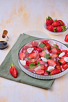 Seasonal salad with strawberries, tomatoes, soft cheese and chives flowers in a white plate on a light concrete background.