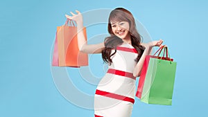 Seasonal sales. Beautiful shopaholic young girl with lots of shopping bags in hands over blue studio background