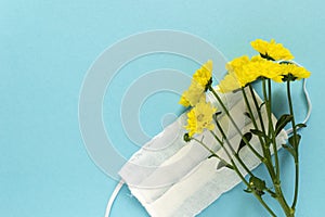 Seasonal spring summer allergy flowers concept. Yellow flowers with medical protective mask on blue background. Creative flat lay