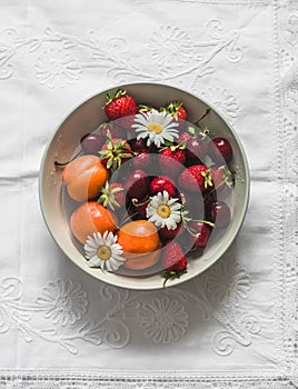 Seasonal summer berries and fruits - apricots, strawberries, cherries in a bowl on a light background, top view