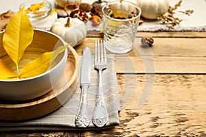 Seasonal table setting with pumpkins and other autumn decor on wooden background, closeup.