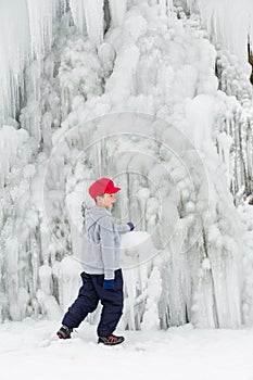 Seasonal winter mood, attractive frozen waterfall, iciles, young boy in red cap plays.