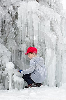 Seasonal winter mood, attractive frozen waterfall, iciles, young boy in red cap plays.