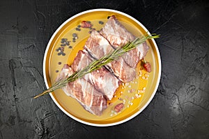 Seasoned fresh raw pork ribs on orange plate on black, top view