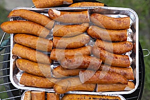 The seasoned and incised sausage lying on an aluminum tray, on a managing grill, in the home garden.