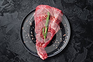 Seasoned raw tri-tip beef meat steak on plate. Black background. Top view