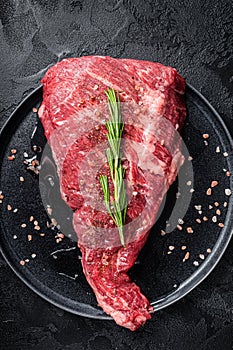Seasoned raw tri-tip beef meat steak on plate. Black background. Top view
