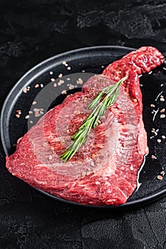 Seasoned raw tri-tip beef meat steak on plate. Black background. Top view