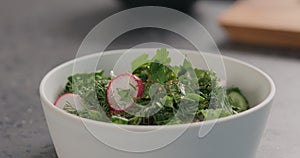 Seasoning fresh salad with radish, cucumber and herbs in white bowl