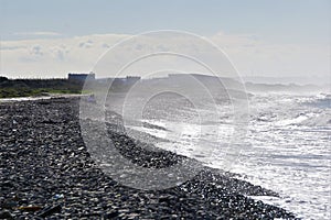 Seaspray fogs stony beach as friends look out to sea