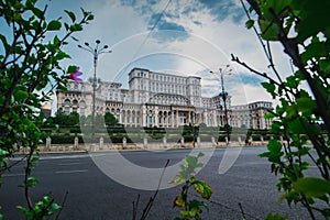 Seat of Romanian parliament, huge building in the centre of Bucharest, Romania on a cloudy summer day. View through the bushes.