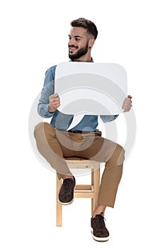 Seated arrogant man holding blank message sign while looking away