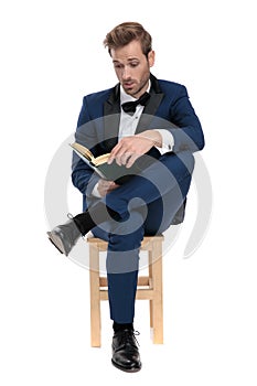 Seated captivated man is reading a book with legs crossed