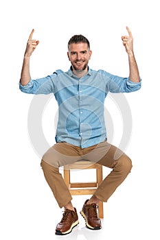 Seated casual guy with beard and grizzled hair pointing fingers up