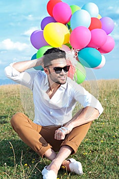 Seated casual man with balloons scratches head