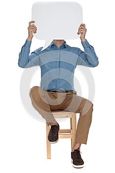 Seated casual man covering his face with empty talk billboard