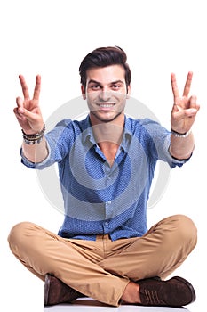 Seated casual man making the victory sign and smiles