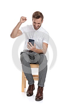 Seated casual man reading good news on his mobile phone