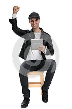 Seated casual man with tablet raising fist victoriously