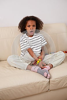Seated comfortably, a yawning and tired mixed race girl is working on a bead craft, dressed in striped shirt, showing a