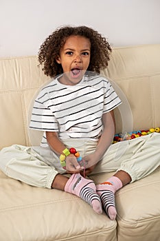 Seated comfortably, a yawning and tired mixed race girl is working on a bead craft, dressed in striped shirt, showing a