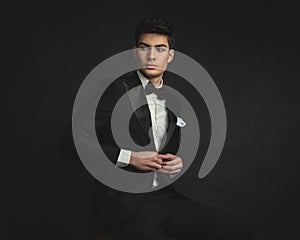 seated gentleman buttoning his black tuxedo and looking to side