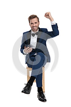 Seated gentleman celebrating victory while holding a mobile phone