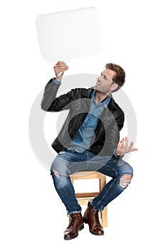 Seated man holding speech bubble sideways mystified