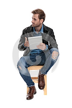 Seated man with tablet looking sideways cocky photo