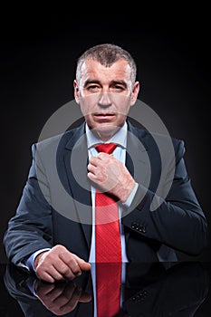 Seated senior business man is fixing his tie