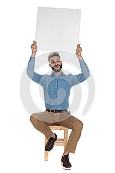 Seated stupid man holds empty billboard in the air