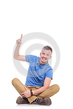 Seated young casual man points upwards