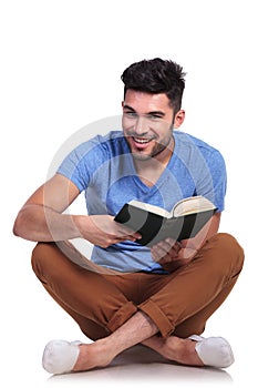 Seated young casual man reading a book and smiles