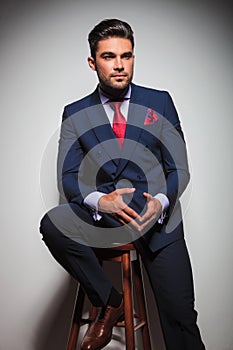 Seated young elegant man in suit and tie looking away