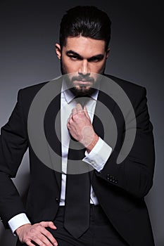 Seated young fashion man fixes his tie