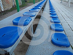 Seats and benches on the sports ground. Plastic blue seats for spectators and fans, empty, no people