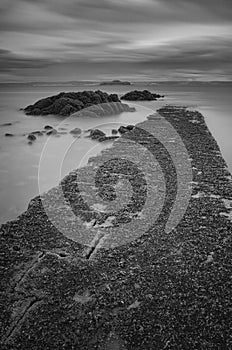 Seaweed covered causeway disappearing into a calm sea by a rocky out crop