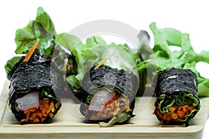 Seaweed salad roll with fresh vegetables and crab stick on wooden plate and white background