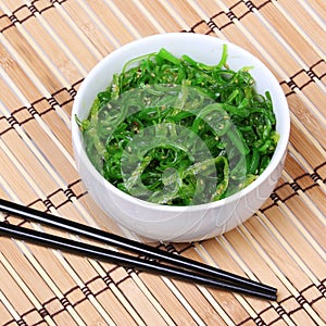 Seaweed with sesame seeds with chopsticks in ceramic bowl on bamboo mat. Chuka salad.