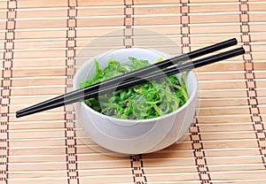 Seaweed with sesame seeds with chopsticks in ceramic bowl on bamboo mat. Chuka salad.