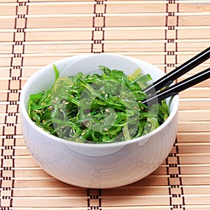 Seaweed with sesame seeds with chopsticks in ceramic bowl on bamboo mat. Chuka salad.