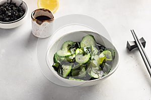 Seaweed wakame salad with cucumber in bowl on gray background.