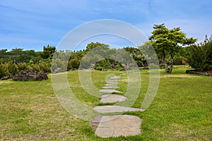 Secluded area with rocky steps, grass, and trees with blue sky in Camellia Hill of Jeju Island, South Korea.