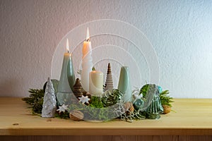 Second Advent, decoration with four different candles, two are lit, green glass Christmas balls, moss and cinnamon stars on a