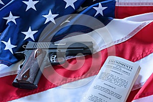 The second amendment and gun control in the US, concept. A handgun and the american constitution on the USA flag.