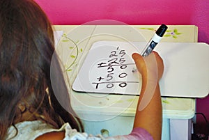 Second grade girl learning how to carry the one on a whiteboard while distance learning not common core math