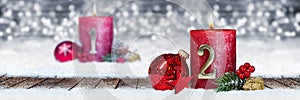 second sunday of advent red candle with golden metal number one on wooden planks in snow front of panorama bokeh background